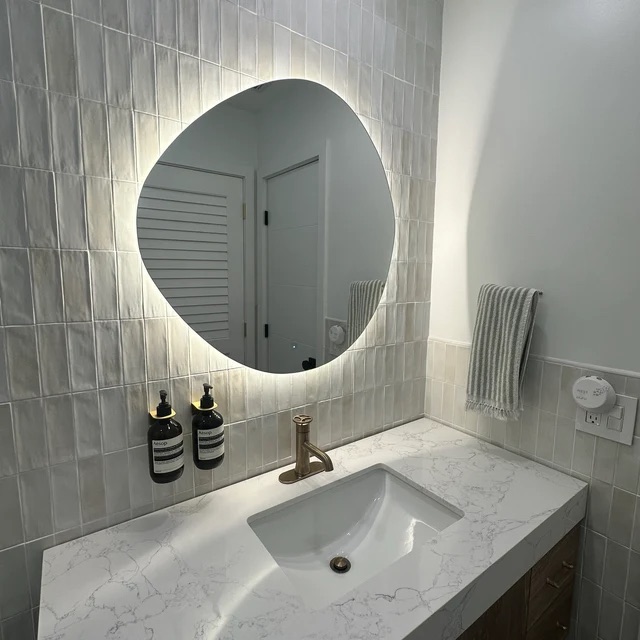 Fotografía de espejo orgánico retroiluminado con luz cálida sobre lavabo
